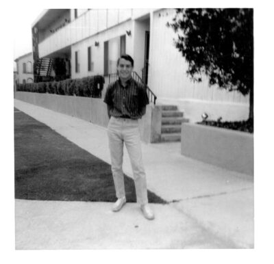 A teenage Gene Brody posing for a photo in front of an apartment building.